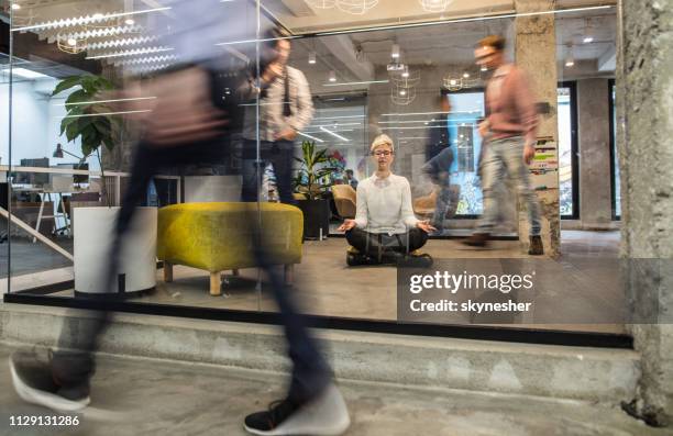 young female entrepreneur meditating with eyes closed in busy office. - office floor stock pictures, royalty-free photos & images