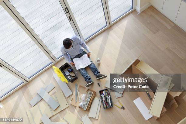 man sat on floor surrounded by flat pack furniture - furniture instructions stock pictures, royalty-free photos & images