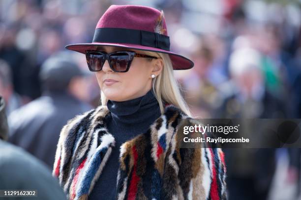 joven elegante con un sombrero de plumas púrpura elegido en foco contra la multitud de personas caminando hacia el hipódromo de cheltenham gold cup día en marzo - cheltenham races fotografías e imágenes de stock