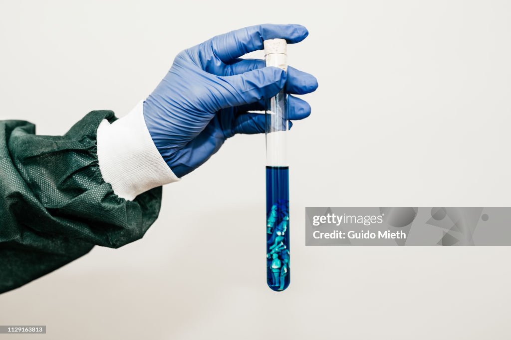 Laboratory worker holding a test tube with little figurines in it.