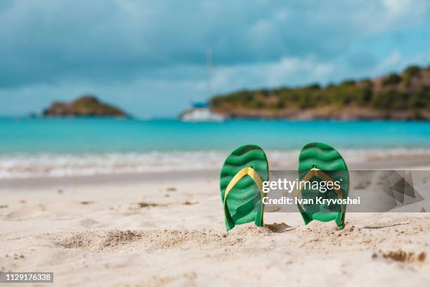 green flip flops in the white sandy beach near sea waves, nobody. summer vacation concept with blue water. relax, vacation on tropical island - green shoes stockfoto's en -beelden