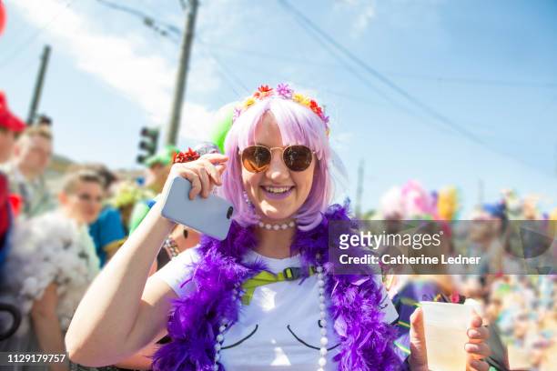 costumed 20 something girl saying hello and holding phone surrounded by party goers - fiesta stock-fotos und bilder