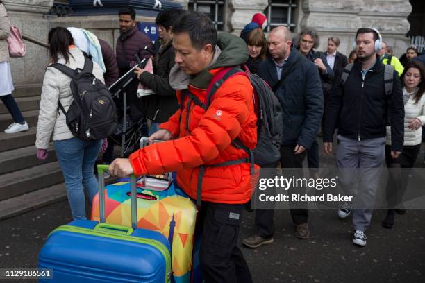 Tourist wheels colourful suitcases negotiates the evening rush-hour alongside ordinary commuters at Waterloo Station, on 4th March 2019, in London...