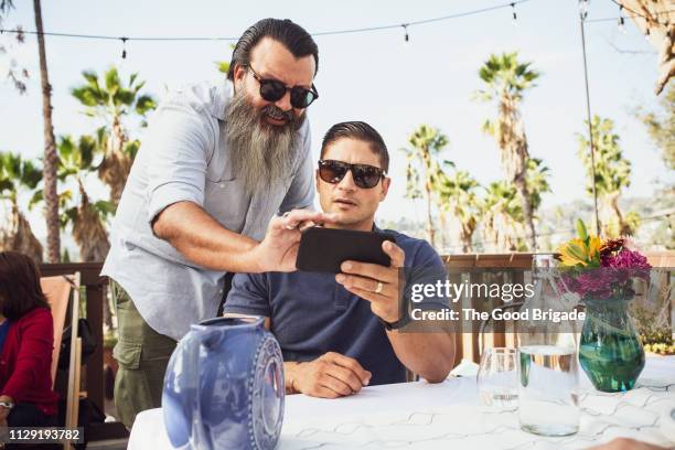 mature men looking at mobile phone together at party - brother in law stock pictures, royalty-free photos & images