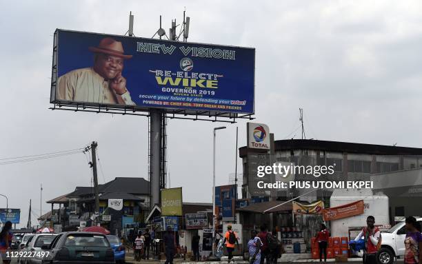 People walk past a campaign billboard of gubernatorial candidate of the Peoples Democratic Party in Rivers State and incumbent Rivers State's...