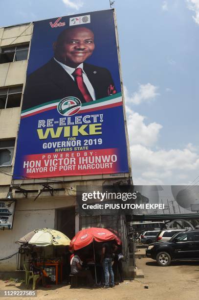 Vendors display their goods at a roadside stall under a campaign billboard of gubernatorial candidate of the Peoples Democratic Party in Rivers State...