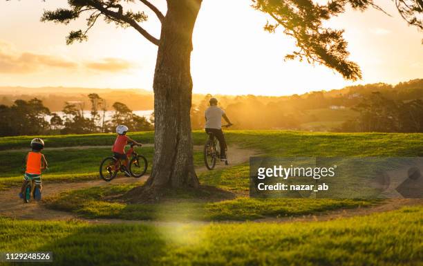 niños siguiendo a papá en bici. - auckland fotografías e imágenes de stock