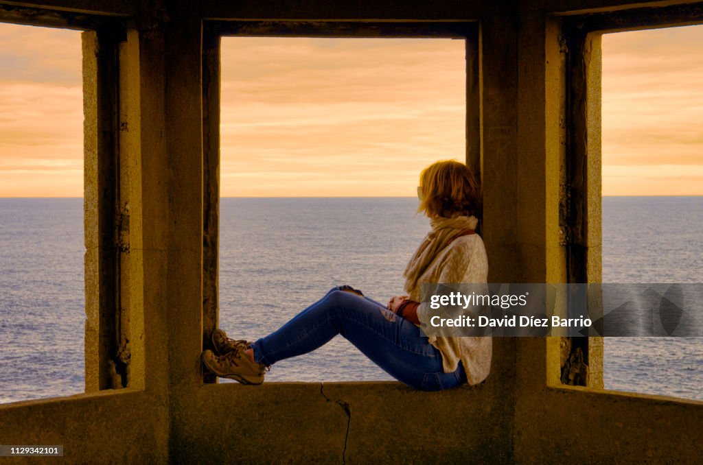 Middle-aged woman sitting in a window enjoying sunset in the Irish sea