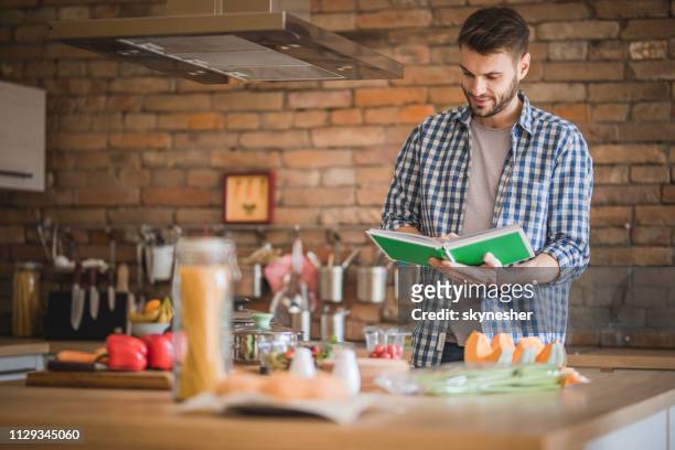 smiling man using cookbook for preparing food in the kitchen. - reading cookbook stock pictures, royalty-free photos & images