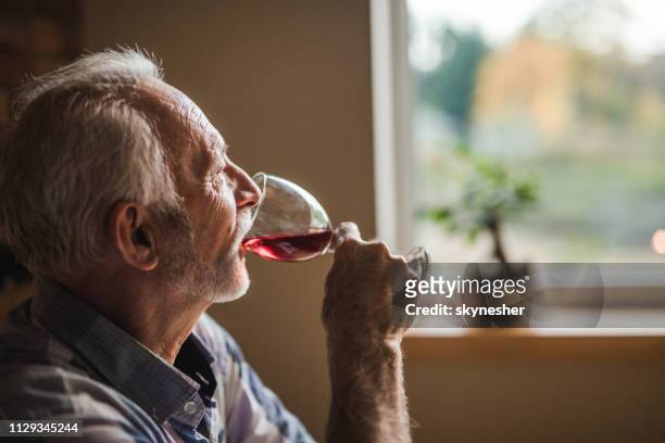 profile view of a senior man drinking wine at home. - men drinking wine stock pictures, royalty-free photos & images