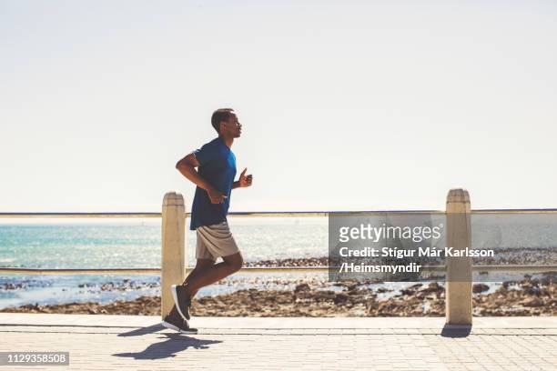 joven atleta hombre corriendo en el paseo marítimo en la playa - sunny side fotografías e imágenes de stock