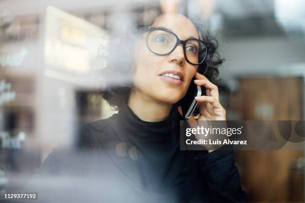 mature woman inside a cafe talking on mobile phone - business telephone stock-fotos und bilder