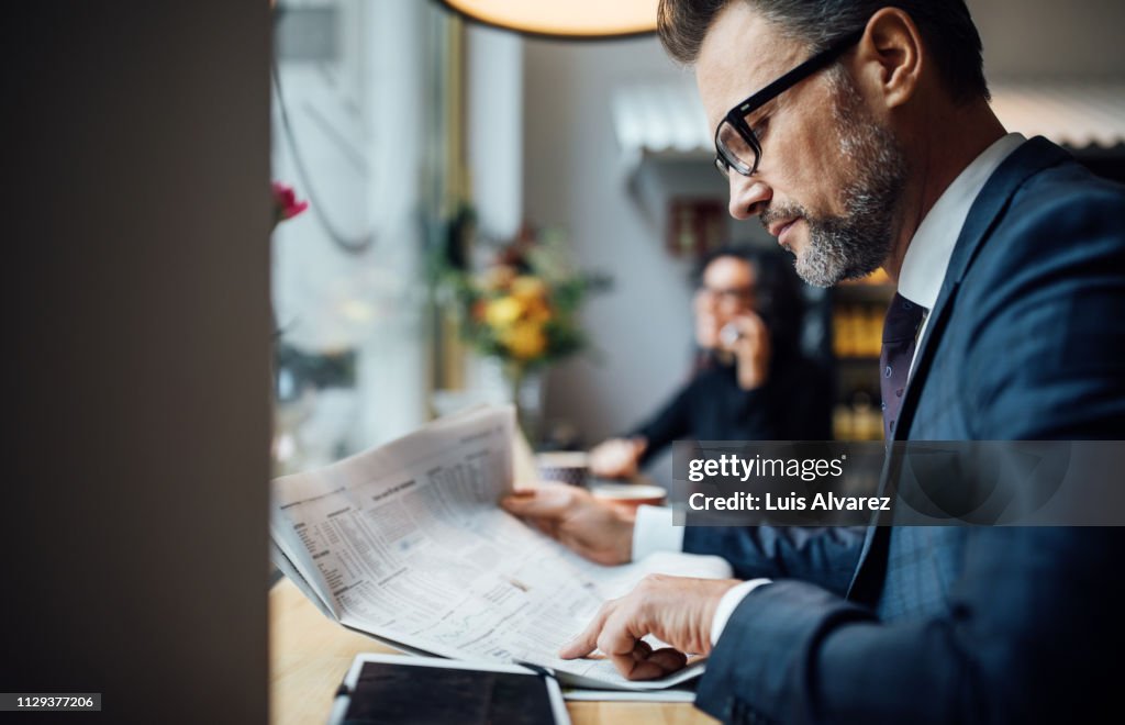Mid adult business professional reading newspaper in cafe