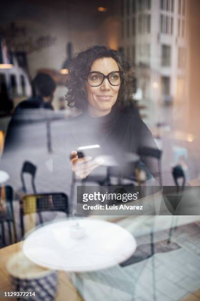 mature woman with a smart phone at coffee shop - media availability stock-fotos und bilder