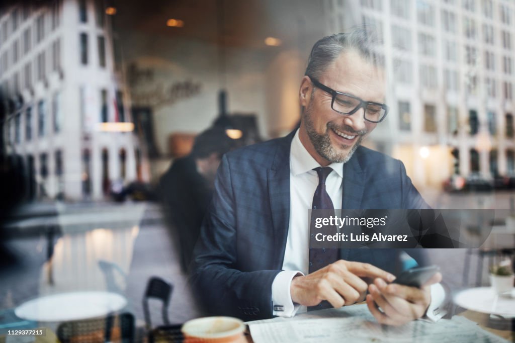 Mature businessman sitting inside at cafe and using phone