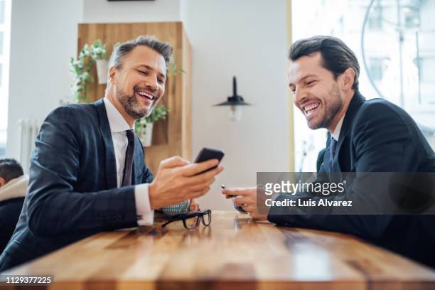 two businessmen at cafe using mobile phone - due persone foto e immagini stock