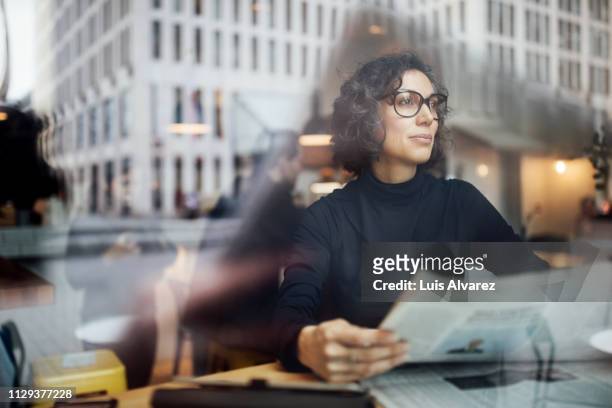 mature businesswoman sitting inside at cafe with newspaper - topnews foto e immagini stock