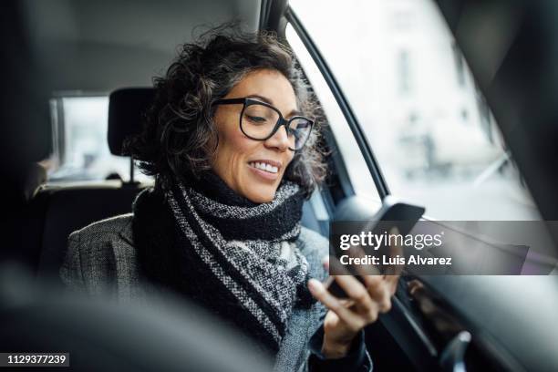 mature businesswoman using phone while traveling by a taxi - accessibility - fotografias e filmes do acervo