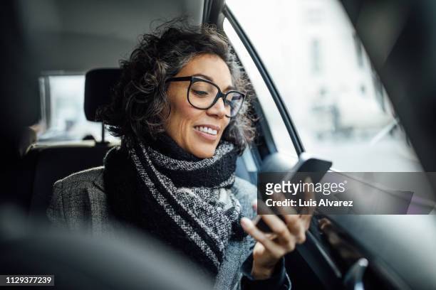 mature businesswoman using phone while traveling by a taxi - passagerarsäte bildbanksfoton och bilder