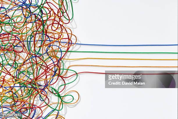 jumble of multicoloured wires untangling into straight lines over a white background. - arrangiare foto e immagini stock