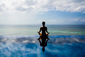 Young woman practicing yoga lotus position on the Infinity pool