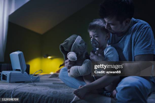 father helping son using nebulizer during inhalation therapy - childhood asthma stock pictures, royalty-free photos & images