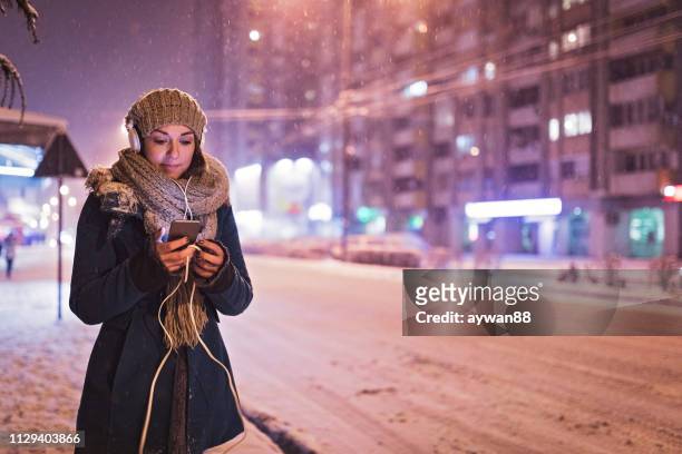 vrouw met behulp van telefoon in besneeuwde buitenshuis - woman snow outside night stockfoto's en -beelden