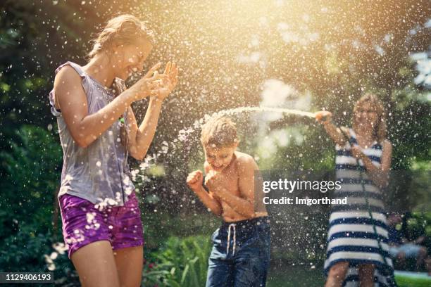 madre che spruzza bambini che ridono nel cortile sul retro - garden hose foto e immagini stock