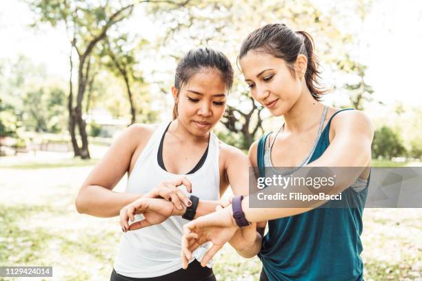 junge frauen, die überprüfung ihrer fitness-tracker im park - fitness tracker stock-fotos und bilder
