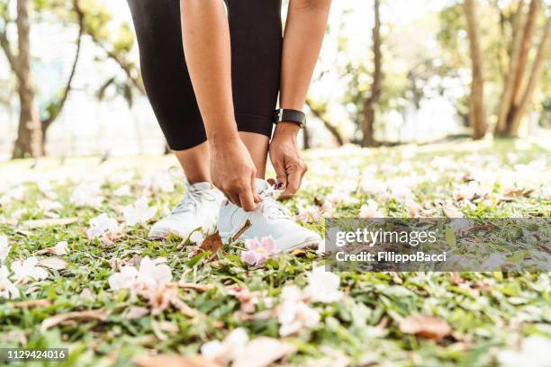 young woman fastening her shoes at the park - lace fastener stock pictures, royalty-free photos & images