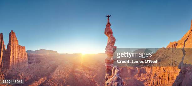 rock climber celebrating on top of summit of climb at sunset, ancient art, moab, usa - successo foto e immagini stock