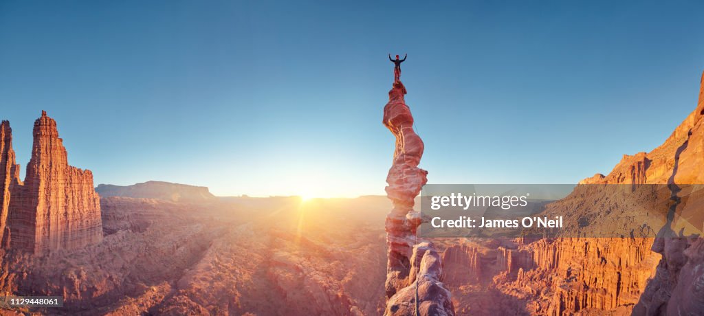 Rock climber celebrating on top of summit of climb at sunset, Ancient Art, Moab, USA