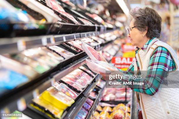 donna anziana che seleziona carne macinata nel reparto carne. - supermarket foto e immagini stock