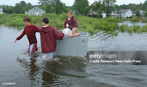Blake Silver and Michael Nickerson use a gray tub to pull Edie Nault and Megan Nickerson through the high water on Poquoson Avenue in Poquoson,...