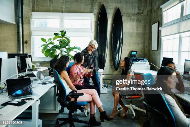 mature female business owner looking at coworkers smart phone while working in design studio - business phone meeting stock pictures, royalty-free photos & images