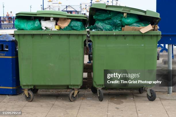 two large overflowing green dumpsters on a sidewalk - müllcontainer stock-fotos und bilder