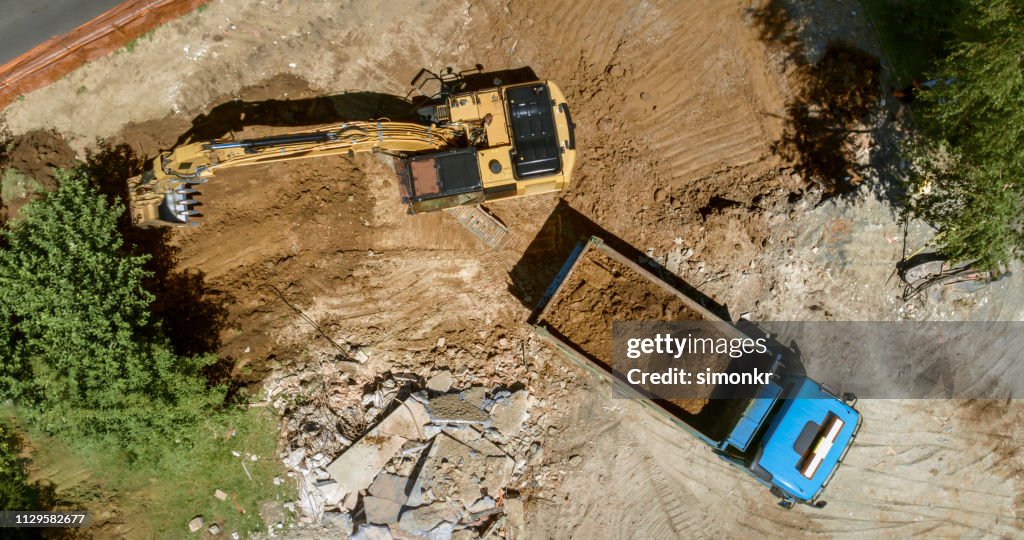 Excavator loading dug out soil onto truck at building site