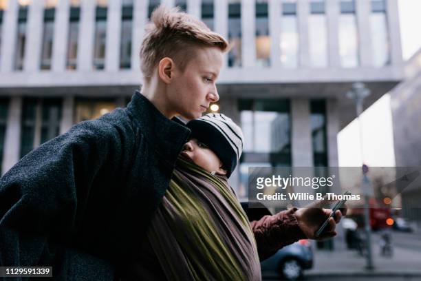 single mother walking with her baby through city - technology on the go stock-fotos und bilder