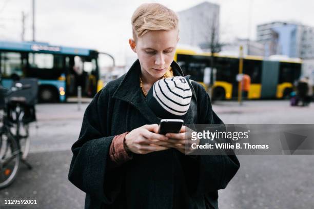 single mother using smartphone while out with baby - androgynous boys stock-fotos und bilder