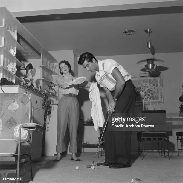 American actress Julie Adams tries to interest her husband Ray Danton in drying the dishes at their home, despite his apparent preoccupation with...