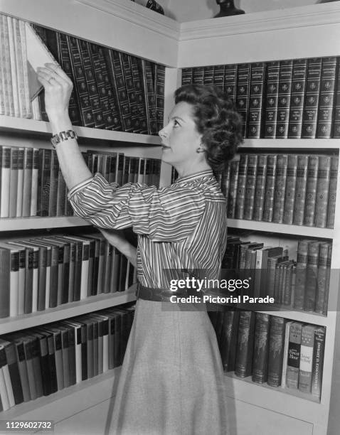 Scottish actress Deborah Kerr taking a book from a shelf at her home, circa 1955.