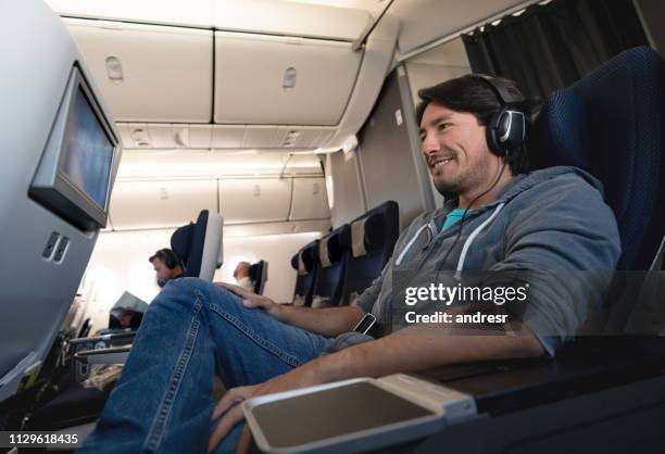 man traveling by plane watching in-flight entertainment using earphones - arts culture and entertainment stock pictures, royalty-free photos & images