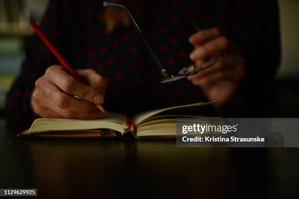 woman writing in a note pad and holding glasses - réfléchir écrire adulte 40 ans papiers photos et images de collection