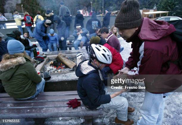 Joe Rong, right, warms the hands of his son, Daniel Rong center, as they take a break alongside the campfire at the Yosemite Outdoor Ice Rink in...