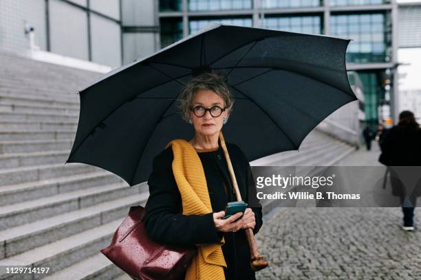 mature woman out on a rainy day - white and black women and umbrella stockfoto's en -beelden