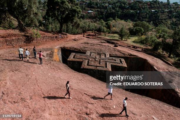 Tourists walk next to the rock-hewn church of Saint George in Lalibela, Ethiopia, on March 6, 2019.