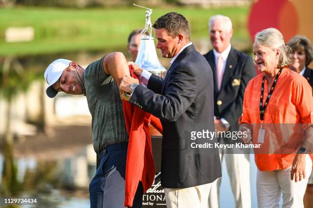 Sam Saunders puts a red cardigan on Francesco Molinari of Italy during the trophy ceremony following his two stroke victory in the final round of the...