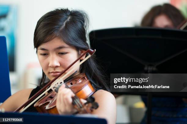 mixed-ethnic teenaged girl playing violin in group class - violinist stock pictures, royalty-free photos & images