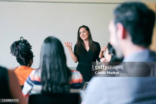 happy teacher gesturing and explaining students in classroom - langue photos et images de collection