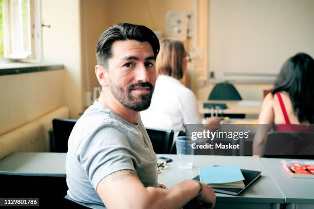 portrait of confident mid adult man sitting in language school - student visa stockfoto's en -beelden